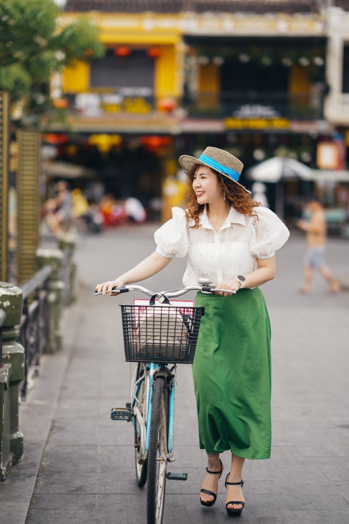 pexels-photo-16567735 Smiling woman with bicycle on city street in summer, enjoying leisure time outdoors.